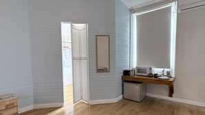 Een kamer met lichtblauwe muren, een houten vloer, een kleine kitchenette met een magnetron, een koelkast en een houten plank.