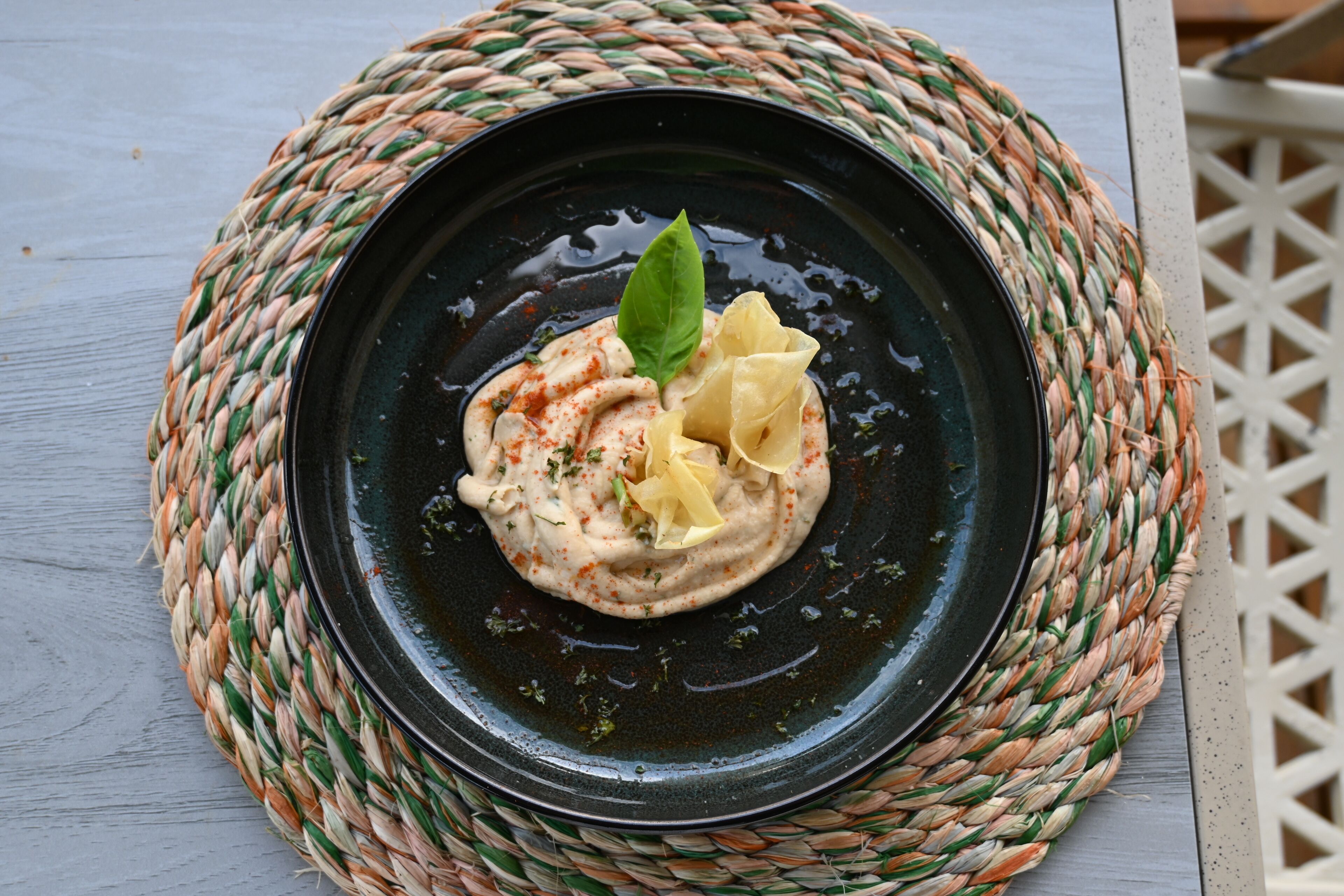 Un plato negro con un guiso cremoso, decorado con una hoja y rodajas de limón, sobre un tapete tejido.