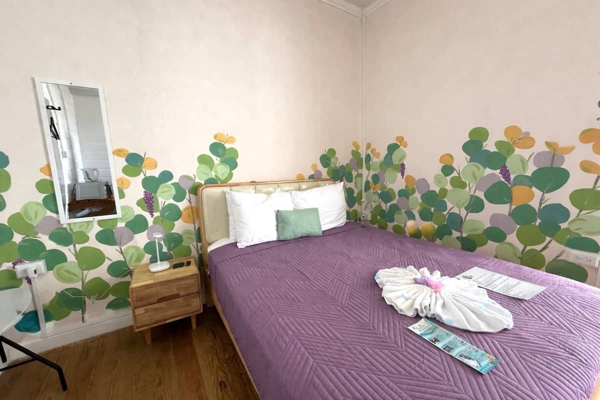 A bedroom with a bed, a nightstand, a mirror, and a wall with a leaf pattern.