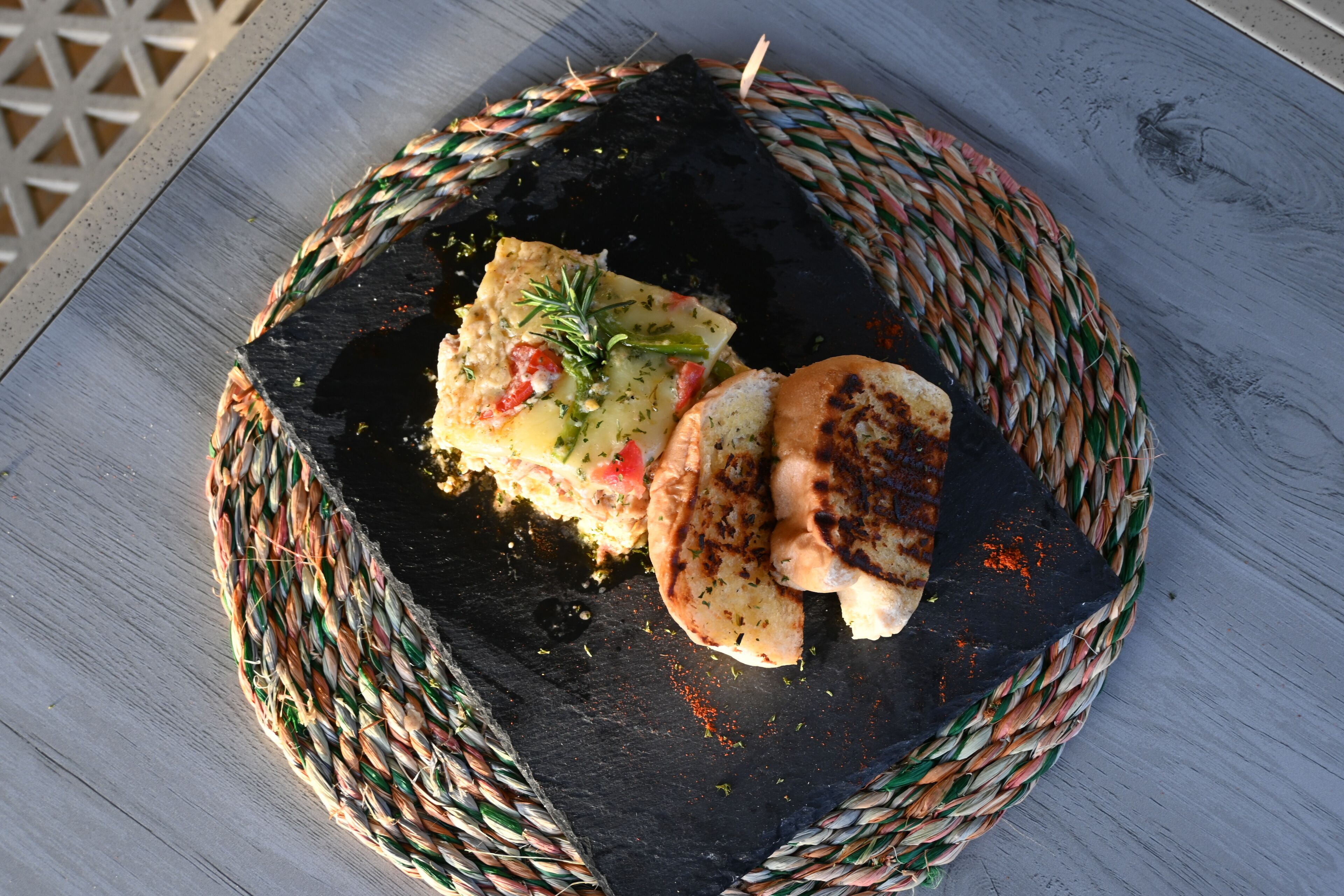 Uma cesta de palha com um prato contendo uma fatia de pão grelhado e queijo, decorado com ervas.
