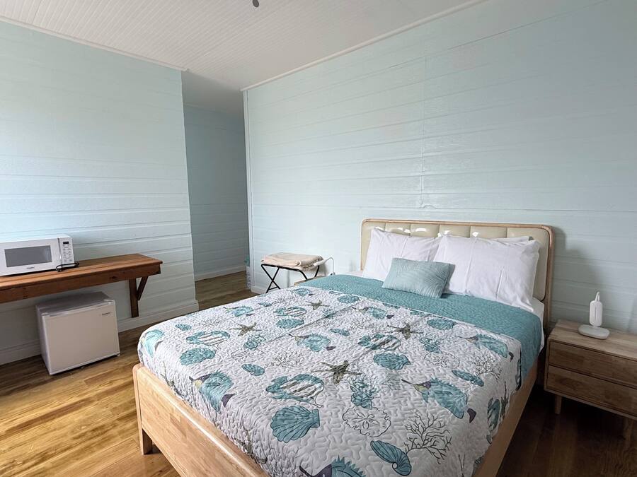 Una camera da letto con un letto in legno, un comodino, una scrivania con un forno a microonde e un piccolo armadietto bianco.