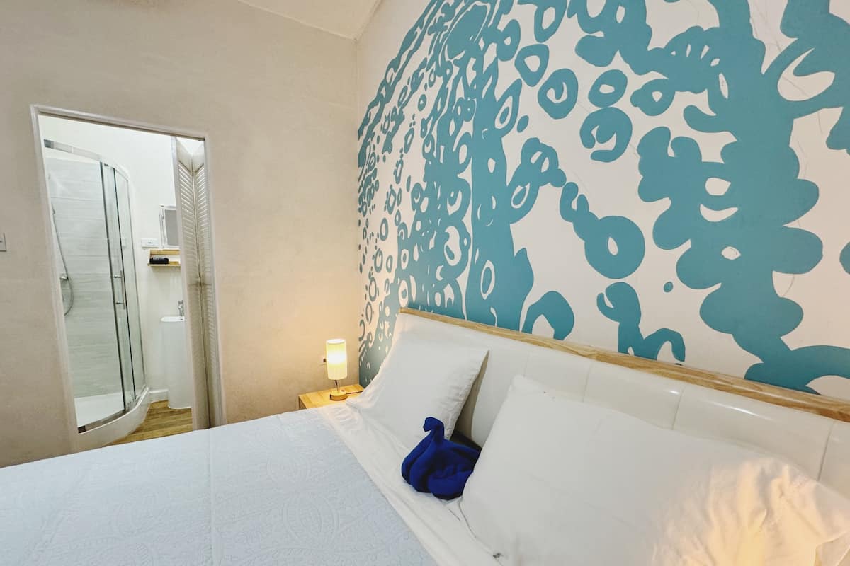 A hotel room with a bed, a shower, and a wall with a blue abstract pattern.