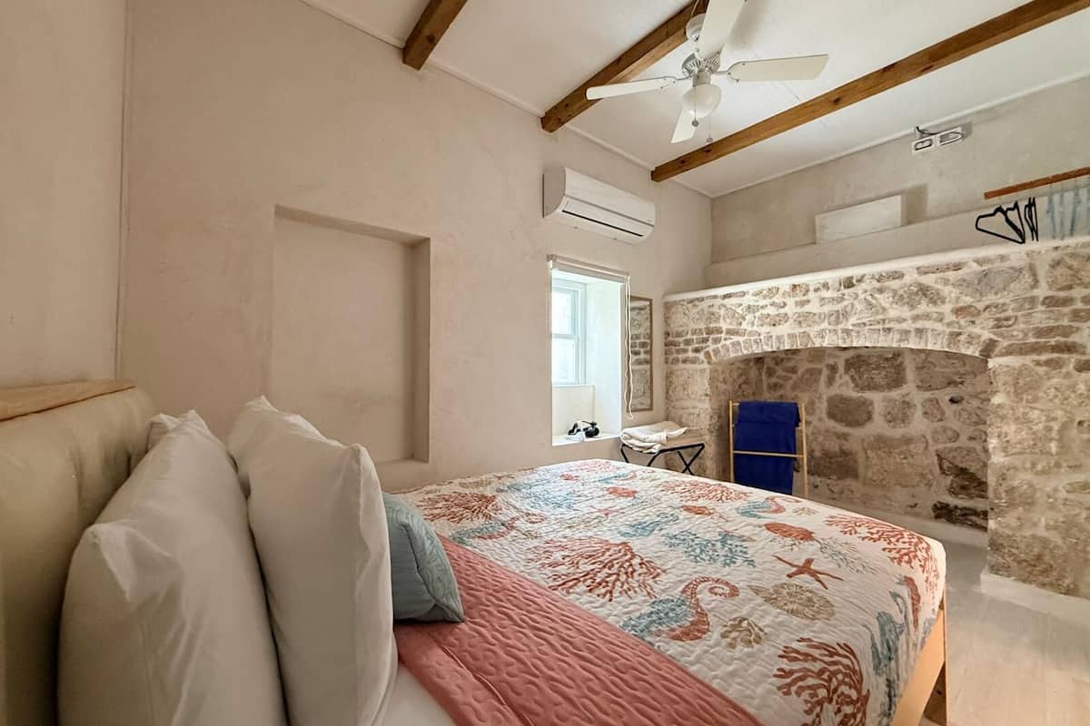 A bedroom with a bed, a stone fireplace, a ceiling fan, and a window.