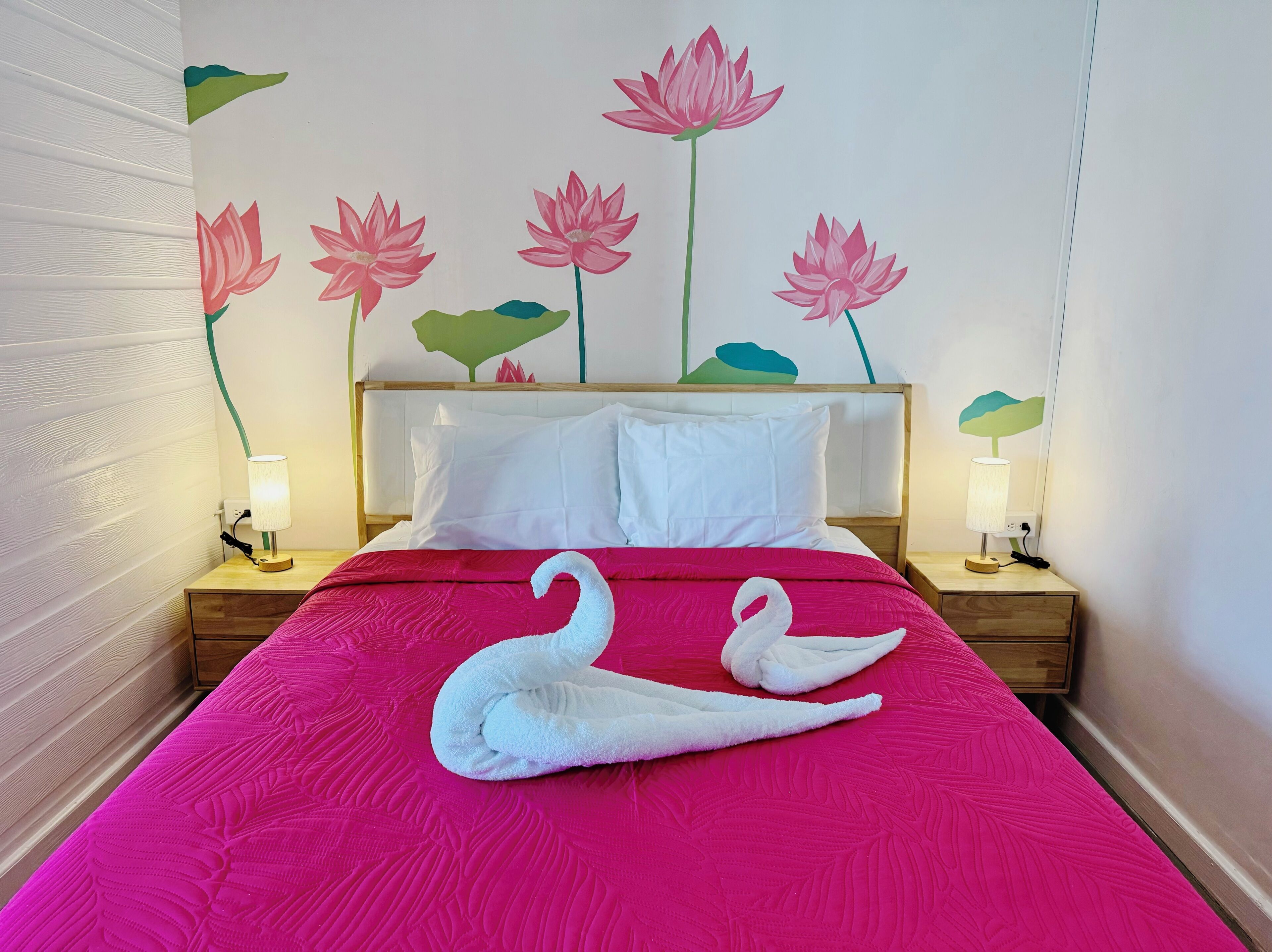 A hotel room with a bed, pillows, a nightstand, a lamp, and a wall mural of flowers.