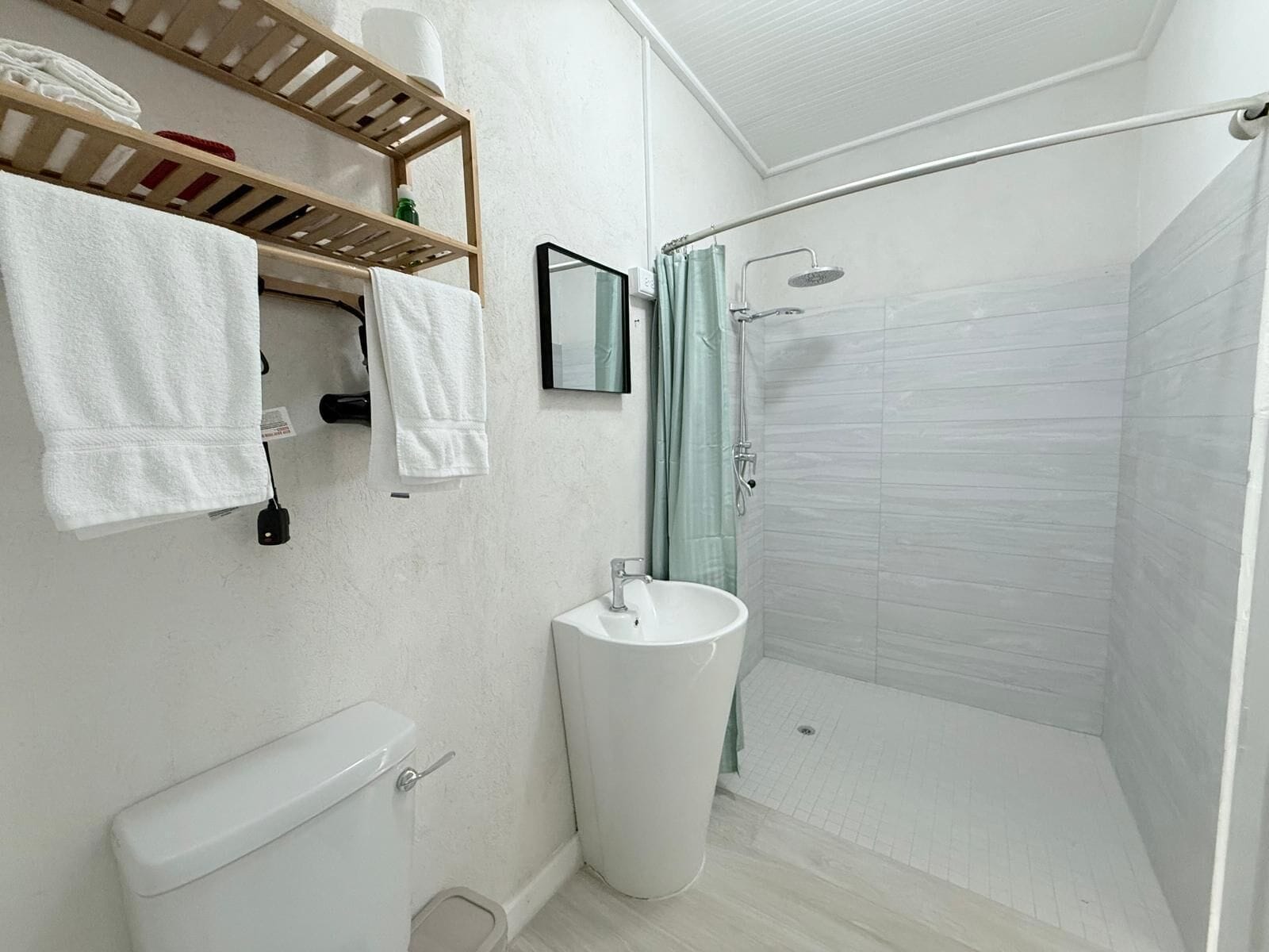 Un baño moderno con inodoro, lavamanos y ducha. Hay toallas y artículos de aseo en un estante.