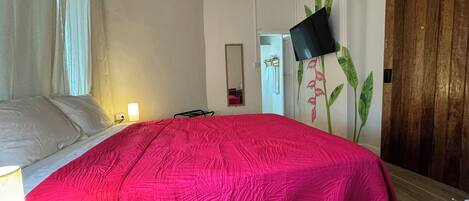 Een slaapkamer met een bed, een flatscreen televisie aan de muur, een houten deur en een spiegel.
