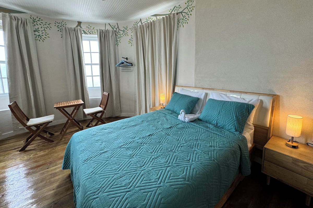 A neatly arranged bedroom with a bed, a chair, a small table, and a nightstand with a lamp.