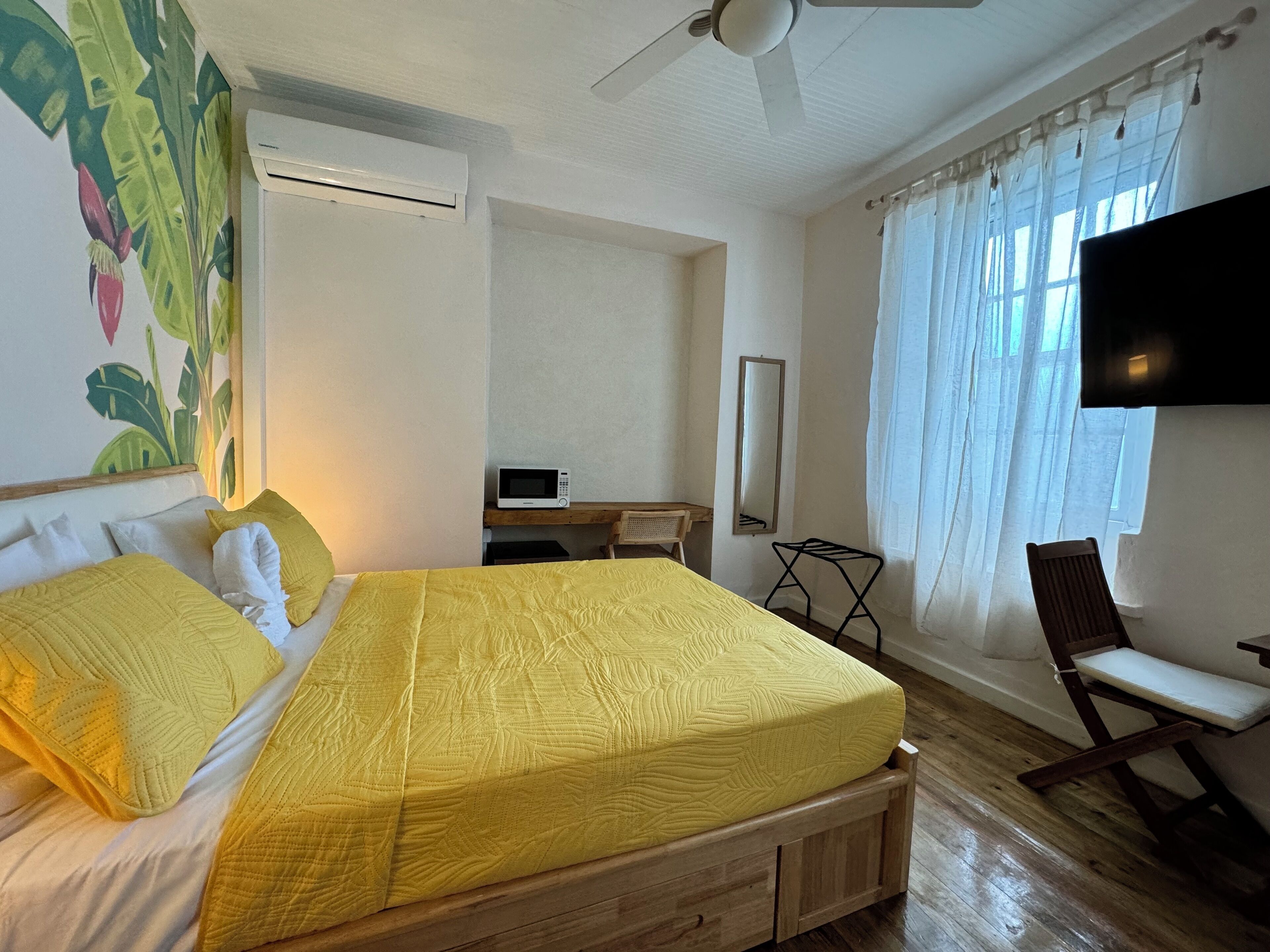 Una habitación con cama, escritorio, silla, televisor y ventilador de techo.