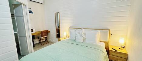 Habitación de hotel con una cama, una mesita de noche de madera, una lámpara de noche, una silla, un escritorio, un espejo y un armario.