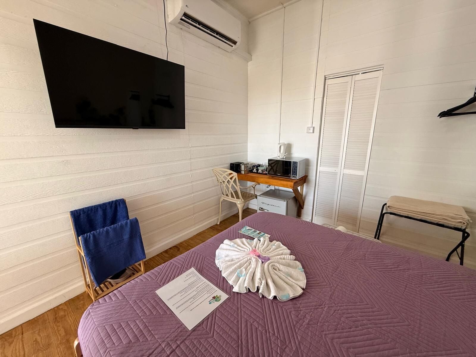A room with a bed, a desk with a computer and a microwave, a chair, and a TV mounted on the wall.