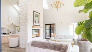A spacious living room with a stone accent wall, a fireplace, and a large window. - Ultra-Luxe Escape | Sleeps 16 | Minutes to RT (Carmine)