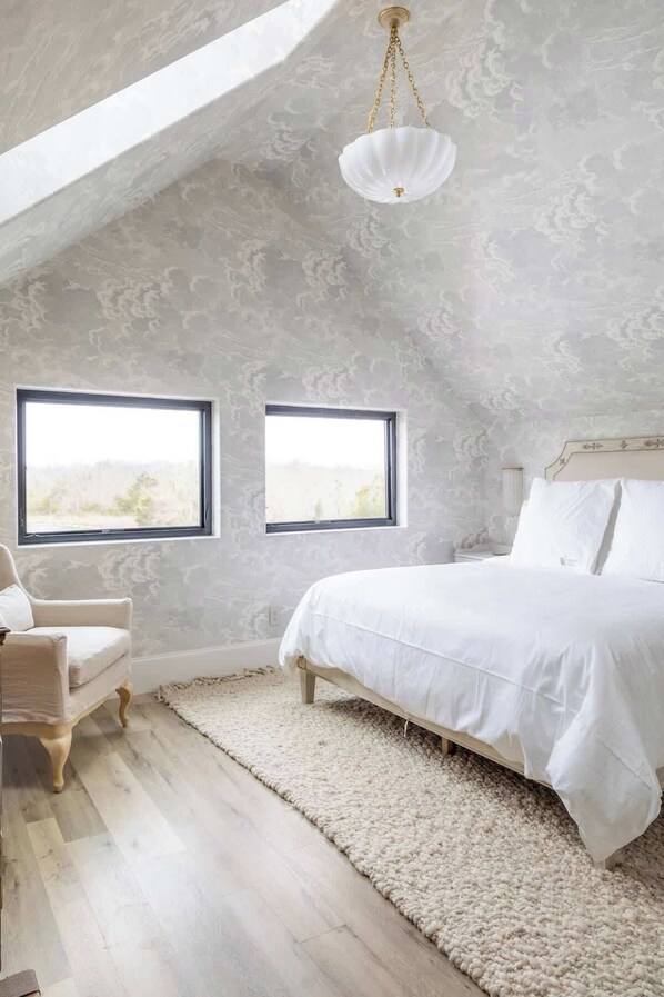 A bedroom with a sloped ceiling, two windows, a bed, a chair, and a fluffy rug. - Ultra-Luxe Escape | Sleeps 16 | Minutes to RT (Carmine)