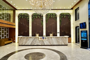 Zona de recepció d'hotel amb un taulell de marbre, un penjador de cristall i una recepció.