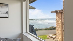 Una habitación con vista al océano a través de una ventana, un sofá gris y un cuadro en la pared.