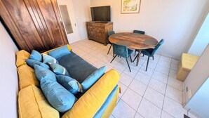 Un salon avec un canapé, une table à manger en bois et des chaises. On y trouve également un téléviseur posé sur un meuble en bois.