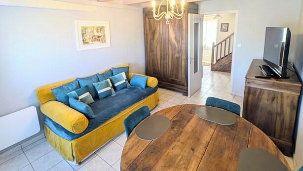 Un salon avec un canapé jaune, une table à manger en bois avec des chaises et un lustre.