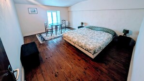 Une chambre à coucher avec un grand lit, une petite table avec des chaises, une fenêtre et une porte.
