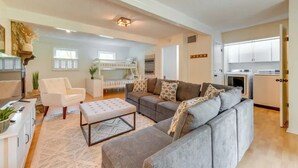 A modern living room with a grey sofa, white armchair, and ottoman. There is a kitchen area with white cabinets and appliances. - Pet-Friendly Lake Norman Retreat (Mooresville)
