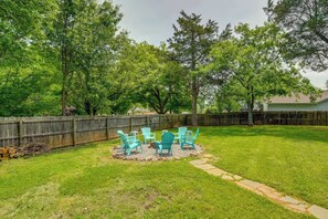 A backyard with a wooden fence, green lawn, and a fire pit with chairs. - Pet-Friendly Lake Norman Retreat (Mooresville)