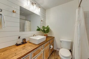 A bathroom with a wooden vanity, a white sink, a mirror with lights, a toilet, and a shower curtain. - Pet-Friendly Lake Norman Retreat (Mooresville)