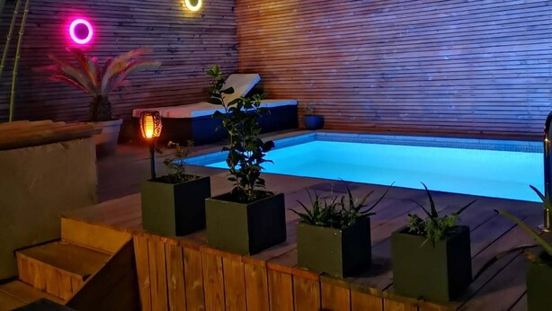 A modern outdoor pool area with a wooden deck, a seating area, and potted plants. - Private room at the foot of the Cevennes (Lodève)
