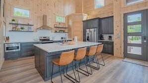 A modern kitchen with wooden walls, a large island with bar stools, and built-in appliances. - Casa Bella: Mtn Views, Movie Room, Games, Hot Tub, Wifi, Yard with Fire Pit! (Sevierville)
