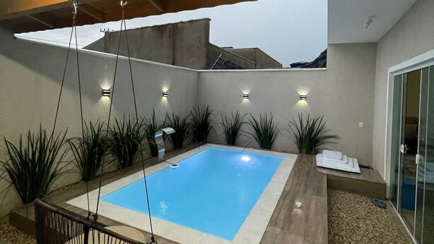 Un área de piscina exterior moderna con una hamaca colgante, rodeada de plantas y una terraza de madera.