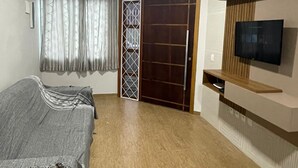Un dormitorio con cama, televisor montado en la pared, piso de madera y puerta con reja de metal.