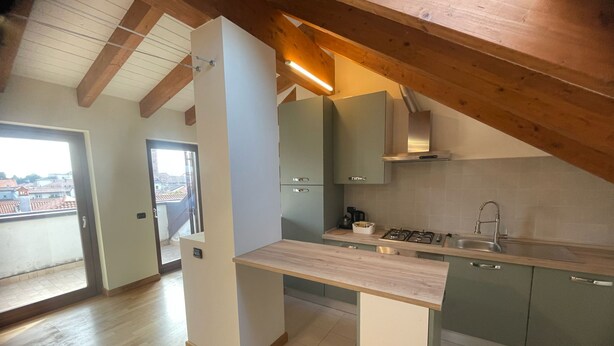 A modern kitchen with wooden beams, a central island, and a view to the outside. - Orchidea Apartment (Seregno)