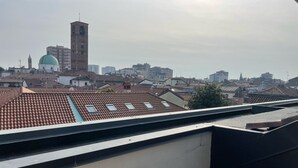A rooftop with terracotta tiles, a white building with a green dome, and a tall tower with a clock. - Orchidea Apartment (Seregno)