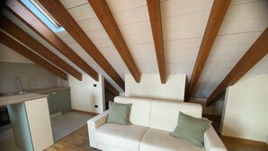 A loft-style room with a wooden ceiling, a white sofa, and a kitchen area. - Orchidea Apartment (Seregno)