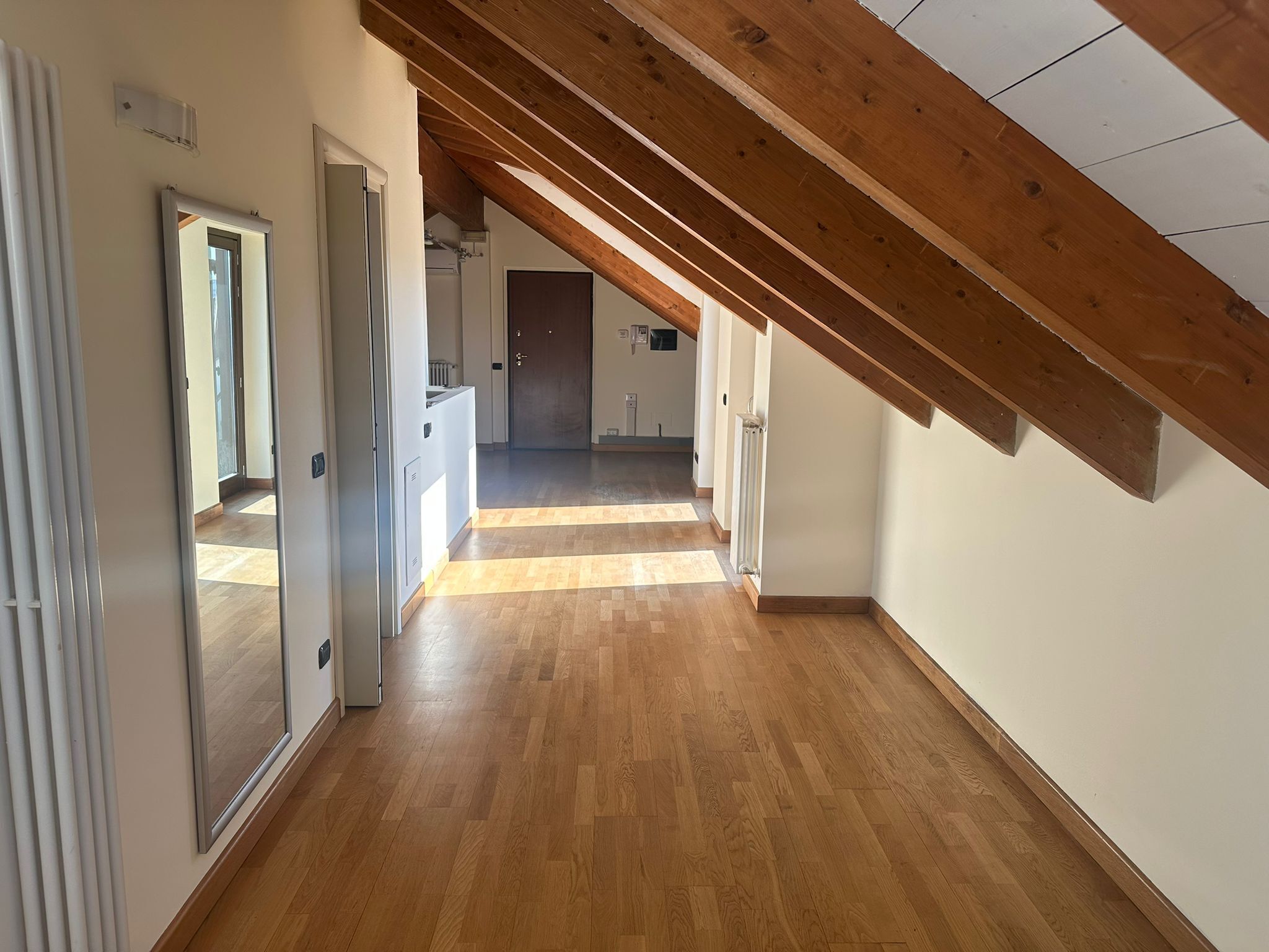 A hallway with wooden flooring and a sloped ceiling.
