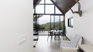 A modern room with a large window, a dining area with a round table and chairs, a sofa, and a unique wall-mounted sculpture.