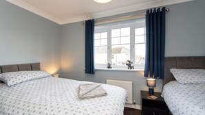 A bedroom with two beds, a window with curtains, a radiator, and a nightstand with a lamp. - Darlington 3 bed House Near Train Station (Darlington)