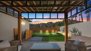 A covered patio with a view of a landscaped backyard, including a putting green and a pool table.