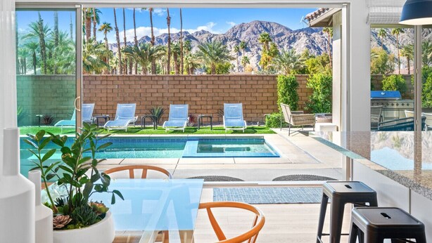 A modern outdoor pool area with lounge chairs and a view of mountains.
