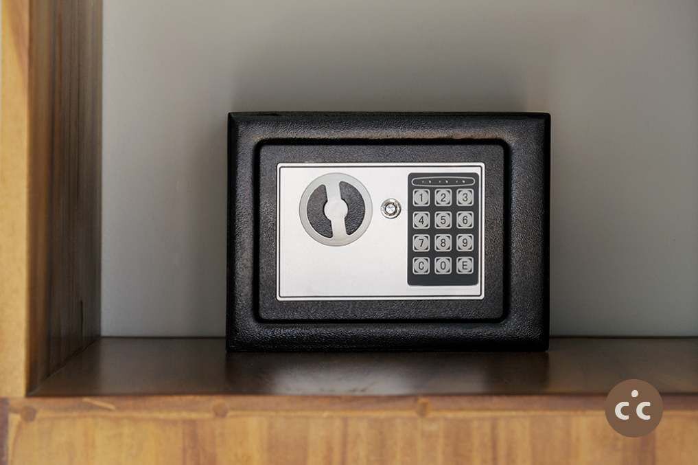 A black safe with a keypad and a combination lock on a wooden shelf.
