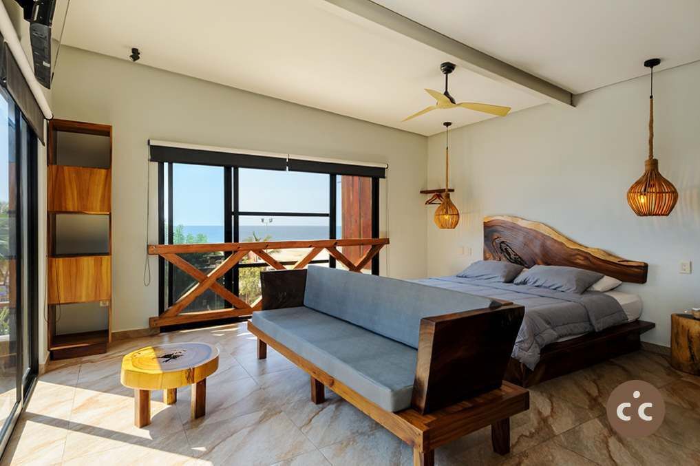 Une chambre avec un grand lit, une tête de lit en bois, un canapé, une petite table ronde et un balcon avec vue.