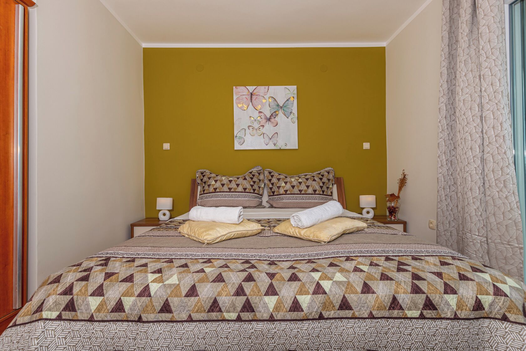 A bedroom with a large bed, two bedside tables, a wall art piece, and a patterned bedspread.