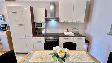 Una cocina moderna con armarios blancos, un microondas, una estufa y un lavamanos. Hay una mesa de comedor con un florero y manteles individuales.