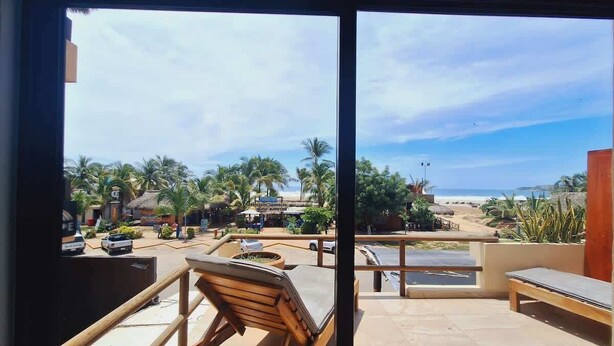 Un espacio al aire libre con sillones de madera y vistas a la playa y palmeras.