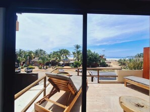 Un espacio al aire libre con sillones de madera y vistas a la playa y palmeras.