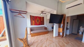 Una habitación con un banco de madera, un ventilador de techo, un televisor montado y un tapiz rojo con estampado.