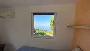 A bedroom with a bed, a window with a view of the sea, and an air conditioning unit on the wall. - Green oasis for 2 with huge private pool + optional guest house | French Riviera (Rayol canadel sur mer)