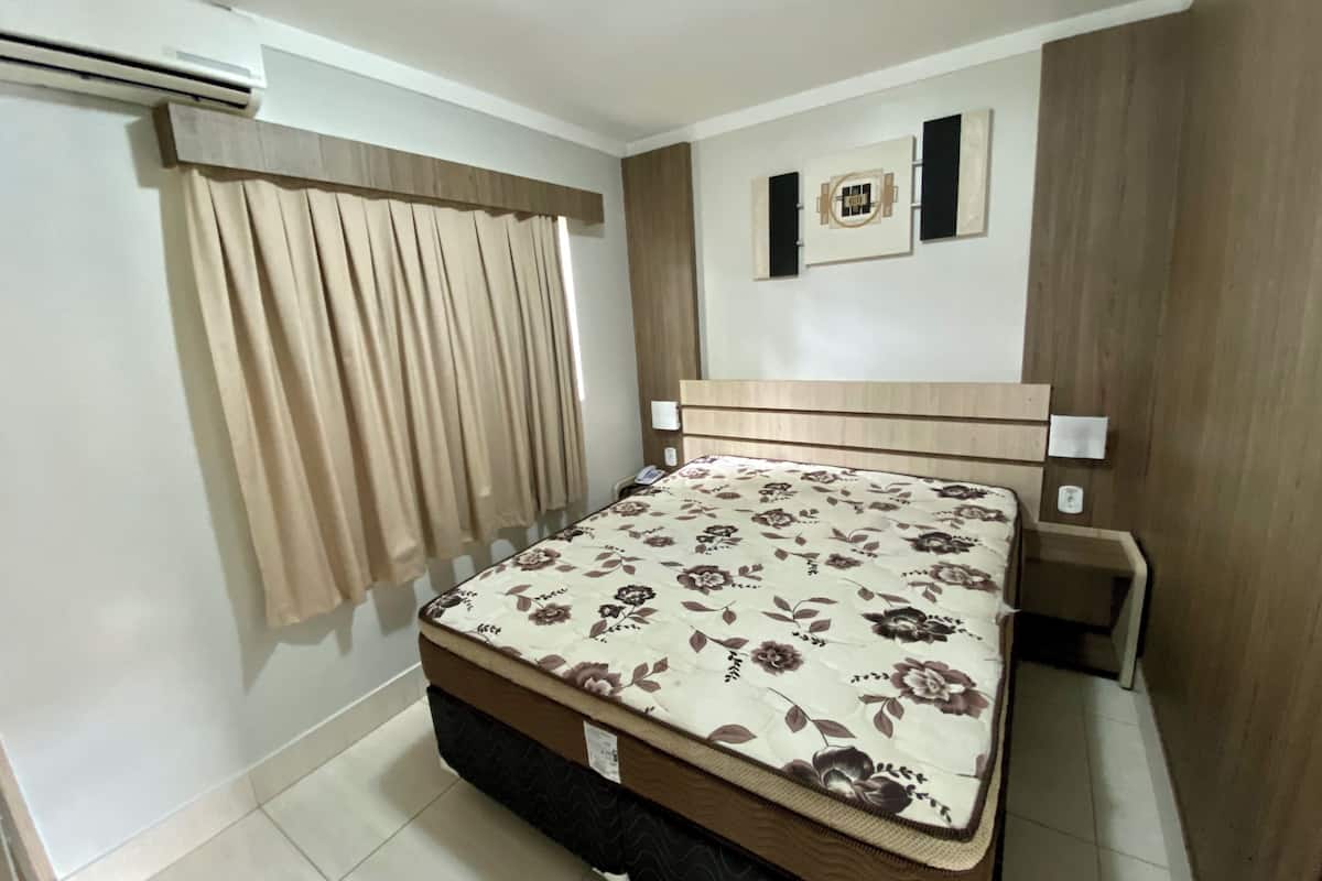 A bedroom with a bed, curtains, a wall-mounted air conditioner, and a small decorative item above the bed.