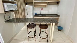 A compact kitchen with a microwave, refrigerator, and a sink. There are two stools at the counter.