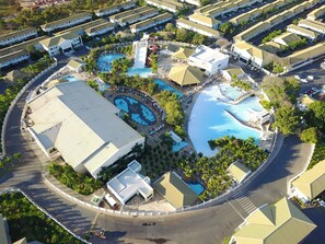 An aerial view of a resort with multiple swimming pools, a water slide, and a variety of buildings with flat roofs.