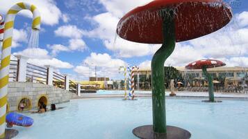 A water park with a large mushroom-shaped water feature, a pool with a bridge, and a building in the background.