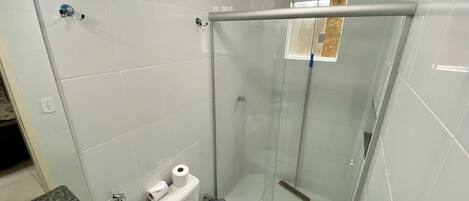 A modern bathroom with white tiles, a glass shower enclosure, a marble countertop, and a toilet with a paper towel holder.