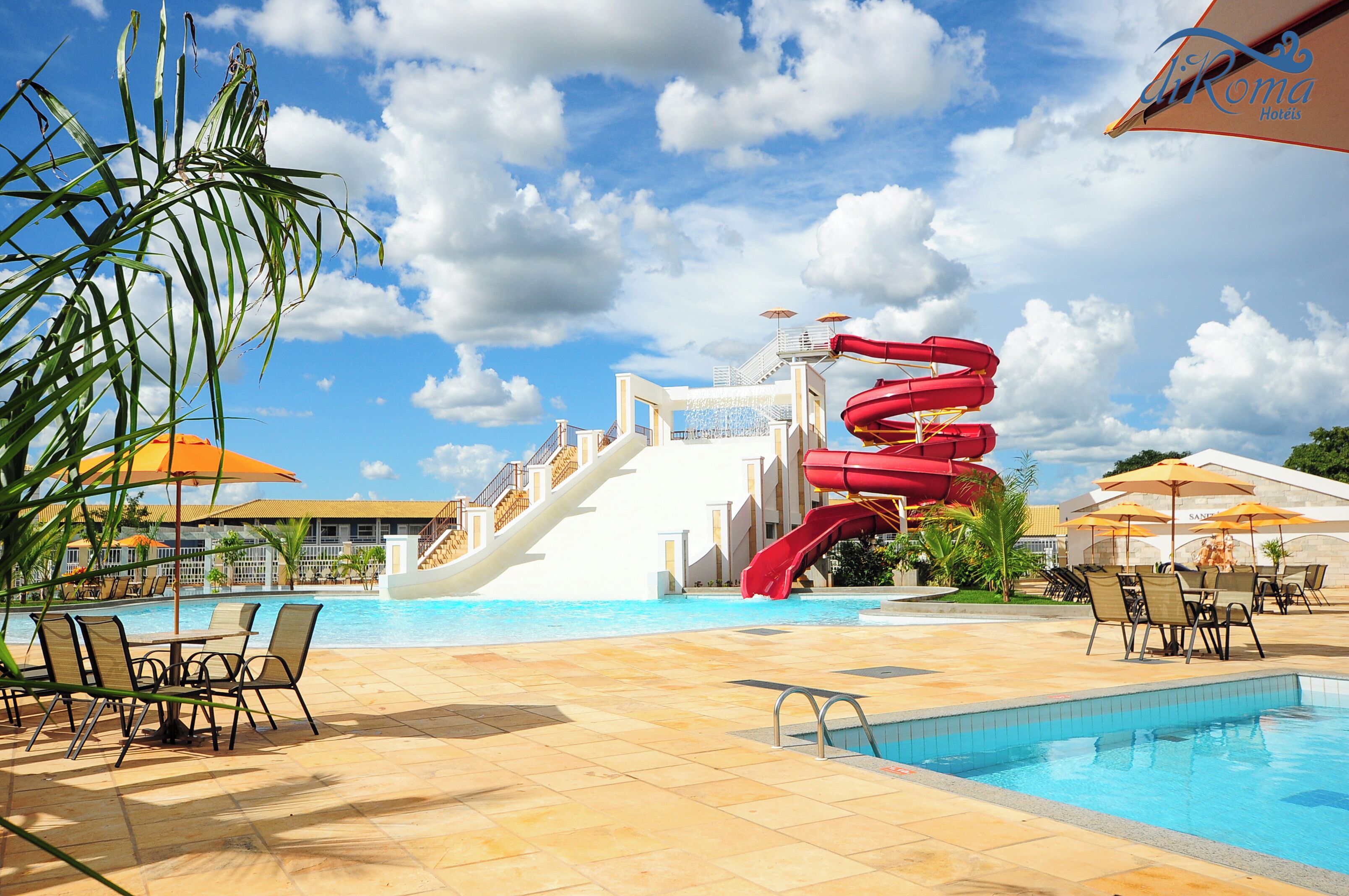 Un área de piscina con tobogán, sillas de descanso y sombrillas.